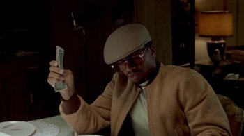 Movie still from “Paid in Full” (2002), directed by Charles Stone III – A man in a tan jacket holding a dollar bill in his hand; Close Up shot, Low angle