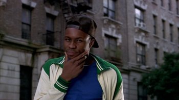 Movie still from “Paid in Full” (2002), directed by Charles Stone III – A man in a baseball cap and jacket standing in front of a building; Close Up shot, Over the shoulder angle