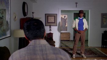 Movie still from “Paid in Full” (2002), directed by Charles Stone III – A man standing in front of another man in a living room; Wide shot, Over the shoulder angle