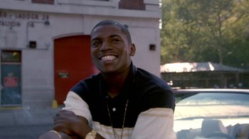 Movie still from “Paid in Full” (2002), directed by Charles Stone III – A young man smiling for the camera while sitting in front of a building; Close Up shot, High angle