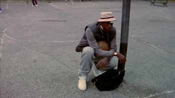 Movie still from “Paid in Full” (2002), directed by Charles Stone III – A man sitting on the ground holding a basketball; Medium shot, Low angle