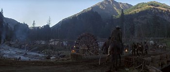 Movie still from “Paint Your Wagon” (1969), directed by Joshua Logan – A group of people riding horses near a wooden wheel; Extreme Wide shot, Low angle