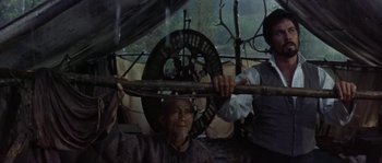 Movie still from “Paint Your Wagon” (1969), directed by Joshua Logan – A man holding a wooden stick over his head while another man stands behind him; Medium shot, High angle