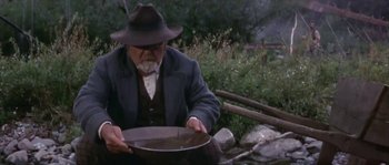 Movie still from “Paint Your Wagon” (1969), directed by Joshua Logan – An old man sitting on a bench holding a pan; Medium shot, High angle