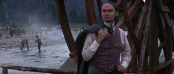 Movie still from “Paint Your Wagon” (1969), directed by Joshua Logan – A man in a vest and tie standing in front of a wooden structure; Medium shot, Low angle