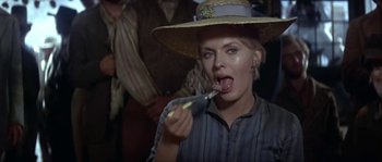 Movie still from “Paint Your Wagon” (1969), directed by Joshua Logan – A woman in a straw hat holding a knife in her mouth; Close Up shot, Low angle