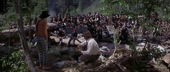 Movie still from “Paint Your Wagon” (1969), directed by Joshua Logan – A group of people sitting in the woods with a man holding a fishing rod; Wide shot, High angle