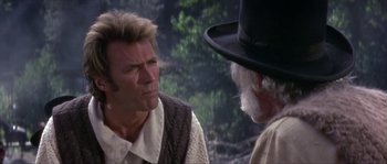 Movie still from “Paint Your Wagon” (1969), directed by Joshua Logan – A man wearing a top hat talking to another man in front of a tree; Close Up shot, Over the shoulder angle