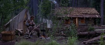 Movie still from “Paint Your Wagon” (1969), directed by Joshua Logan – A man sitting on a chair in the woods near a fire pit; Wide shot, Low angle