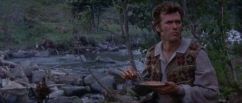Movie still from “Paint Your Wagon” (1969), directed by Joshua Logan – A man holding a plate of food near a river; Medium shot, Low angle