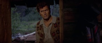Movie still from “Paint Your Wagon” (1969), directed by Joshua Logan – A person wearing a vest near a building; Medium shot, Over the shoulder angle