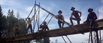 Movie still from “Paint Your Wagon” (1969), directed by Joshua Logan – A group of men sitting on top of a wooden structure; Wide shot, Low angle