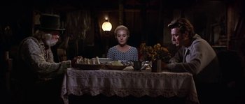 Movie still from “Paint Your Wagon” (1969), directed by Joshua Logan – A woman sitting at a dinner table with two other people; Medium shot, High angle