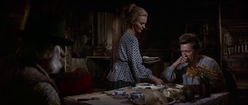 Movie still from “Paint Your Wagon” (1969), directed by Joshua Logan – A woman standing in front of plates of food on top of a table; Medium shot, Over the shoulder angle