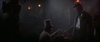 Movie still from “Paint Your Wagon” (1969), directed by Joshua Logan – A man wearing a top hat is sitting at a dinner table; Medium shot, Low angle