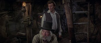 Movie still from “Paint Your Wagon” (1969), directed by Joshua Logan – A man standing next to another man wearing a top hat; Medium shot, Over the shoulder angle