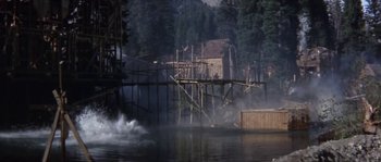 Movie still from “Paint Your Wagon” (1969), directed by Joshua Logan – A body of water near a forest with a wooden bridge; Extreme Wide shot, High angle