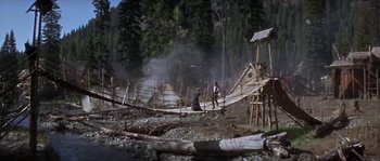 Movie still from “Paint Your Wagon” (1969), directed by Joshua Logan – A group of people walking across a wooden bridge; Extreme Wide shot, High angle
