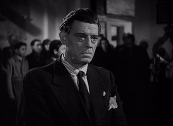 Movie still from “Paisan” (1946), directed by Roberto Rossellini – A man wearing a suit and tie in front of a group of people; Close Up shot, Low angle