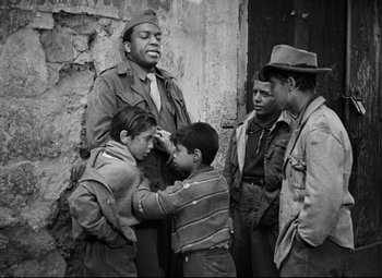 Movie still from “Paisan” (1946), directed by Roberto Rossellini – A group of young men standing next to each other near a building; Medium shot, Over the shoulder angle