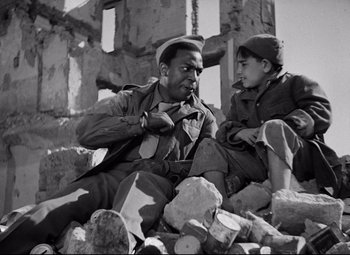 Movie still from “Paisan” (1946), directed by Roberto Rossellini – An old photo of a man and a boy sitting on a pile of rubble; Medium shot, Over the shoulder angle