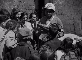 Movie still from “Paisan” (1946), directed by Roberto Rossellini – A group of people gathered around a man reading a book; Medium shot, Over the shoulder angle