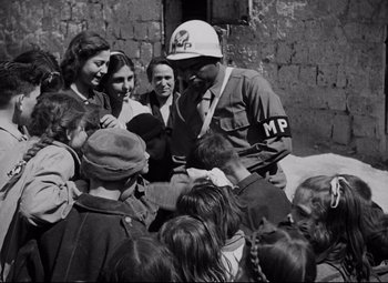 Movie still from “Paisan” (1946), directed by Roberto Rossellini – An old black and white photo of a man in a crowd; Medium shot, Over the shoulder angle