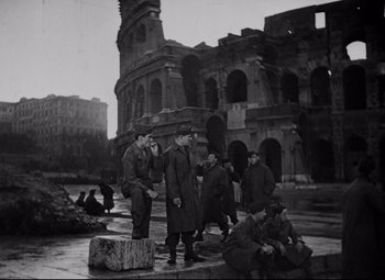 Movie still from “Paisan” (1946), directed by Roberto Rossellini – A black and white photo of men standing in front of an old building; Wide shot, Low angle