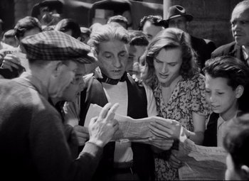 Movie still from “Paisan” (1946), directed by Roberto Rossellini – A group of people standing around looking at papers; Medium shot, High angle