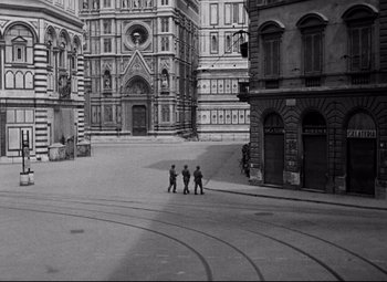 Movie still from “Paisan” (1946), directed by Roberto Rossellini – Three people are standing on the sidewalk in front of a building; Extreme Wide shot, High angle