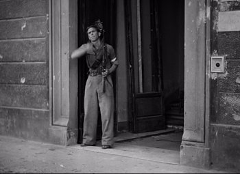 Movie still from “Paisan” (1946), directed by Roberto Rossellini – A man standing in front of a building holding a camera; Medium shot, Low angle