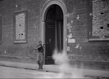 Movie still from “Paisan” (1946), directed by Roberto Rossellini – A black and white photo of a man holding a violin; Wide shot, Low angle