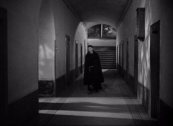 Movie still from “Paisan” (1946), directed by Roberto Rossellini – A man in a black robe walking down a hall way; Wide shot, High angle