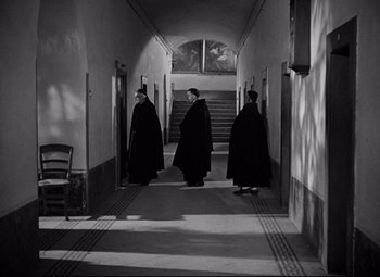 Movie still from “Paisan” (1946), directed by Roberto Rossellini – A group of men in robes walking down a hall way; Wide shot, High angle