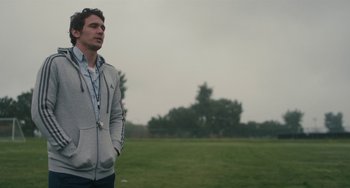 Movie still from “Palo Alto” (2013), directed by Gia Coppola – A man standing in a grassy field with his hands in his pockets; Medium shot, Low angle