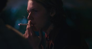 Movie still from “Palo Alto” (2013), directed by Gia Coppola – A young man smoking a cigarette in a dark room; Close Up shot, Over the shoulder angle