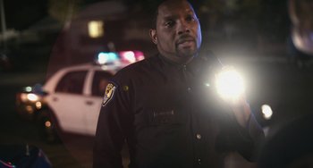 Movie still from “Palo Alto” (2013), directed by Gia Coppola – A police officer is holding a flashlight in his hand; Medium shot, Over the shoulder angle