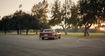 Movie still from “Palo Alto” (2013), directed by Gia Coppola – A man standing next to a red car on a street; Extreme Wide shot, High angle
