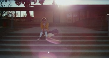 Movie still from “Palo Alto” (2013), directed by Gia Coppola – A person sitting on some steps in the sunlight; Wide shot, Low angle