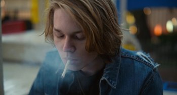 Movie still from “Palo Alto” (2013), directed by Gia Coppola – A young man smoking a cigarette while wearing a jean jacket; Close Up shot, Low angle