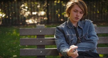 Movie still from “Palo Alto” (2013), directed by Gia Coppola – A man sitting on top of a wooden park bench; Medium shot, Low angle