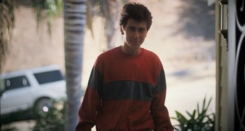 Movie still from “Palo Alto” (2013), directed by Gia Coppola – A man in a red and gray sweater standing next to a palm tree; Medium shot, High angle
