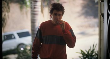 Movie still from “Palo Alto” (2013), directed by Gia Coppola – A man in a red and blue striped sweater smoking a cigarette in front of palm trees; Medium shot, High angle