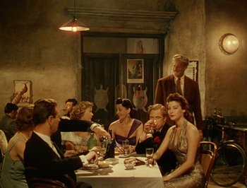 Movie still from “Pandora and the Flying Dutchman” (1951), directed by Albert Lewin – A group of people sitting at a table with food; Wide shot, High angle
