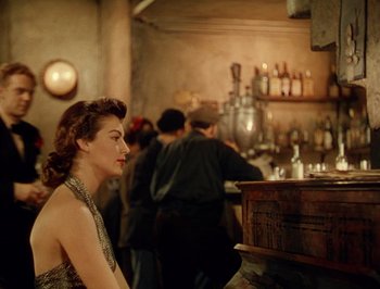 Movie still from “Pandora and the Flying Dutchman” (1951), directed by Albert Lewin – A woman sitting at a table in front of a bar; Medium shot, Over the shoulder angle