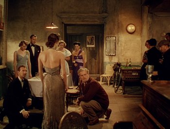 Movie still from “Pandora and the Flying Dutchman” (1951), directed by Albert Lewin – A group of people standing in a room with a man kneeling next to a woman; Wide shot, High angle