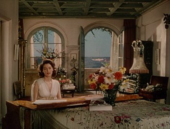 Movie still from “Pandora and the Flying Dutchman” (1951), directed by Albert Lewin – A woman sitting at a table in a room; Wide shot, Low angle