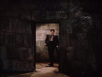 Movie still from “Pandora and the Flying Dutchman” (1951), directed by Albert Lewin – A man in a suit and tie standing in an archway; Wide shot, High angle