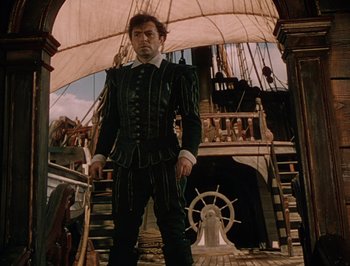 Movie still from “Pandora and the Flying Dutchman” (1951), directed by Albert Lewin – A man standing on top of a boat in front of a ship; Medium shot, Low angle