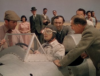 Movie still from “Pandora and the Flying Dutchman” (1951), directed by Albert Lewin – A group of people standing around a man in a plane; Medium shot, High angle